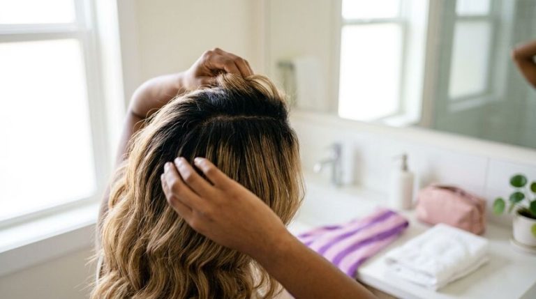 Mulher arrumando cabelo em banheiro iluminado.