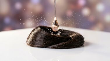 Gota de óleo caindo sobre cabelo sedoso