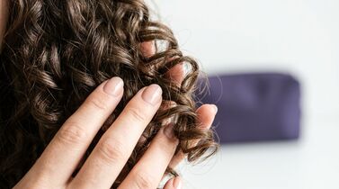 Mão segurando cachos de cabelo castanho