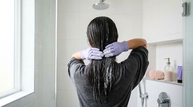 Mulher lavando o cabelo no chuveiro com luvas
