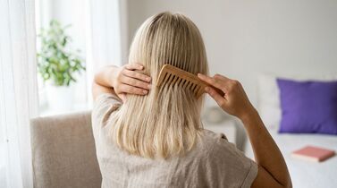 Mulher escovando cabelo loiro com pente de madeira.