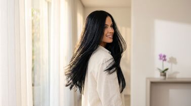 Mulher sorrindo em ambiente iluminado com cortinas
