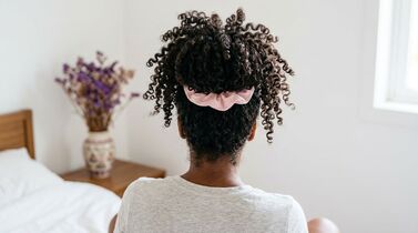 Cabelo cacheado preso com laço rosa.