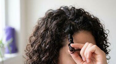 Mulher com cabelo cacheado e dedo segurando um cacho